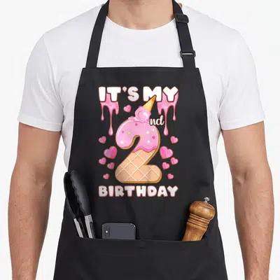 2nd ice cream apron - Number 2 ice cream cone with pink frosting, IT'S MY 2nd BIRTHDAY text, and scattered hearts — shown on a black cotton canvas apron against a white background