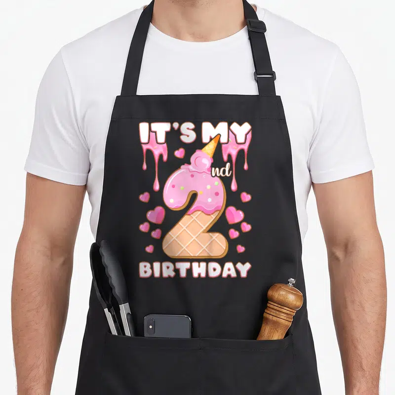 2nd ice cream apron - Number 2 ice cream cone with pink frosting, IT'S MY 2nd BIRTHDAY text, and scattered hearts — shown on a black cotton canvas apron against a white background