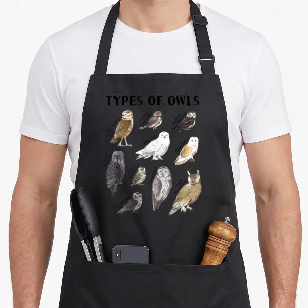Educational owl apron - Eleven realistic owls labeled Burrowing, Snow, Barn, and Great Horned in brown and grey — shown on a black cotton canvas apron against a white background
