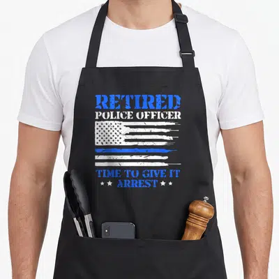 Police modern apron - Distressed flag with blue stripe and text retired police officer time to give it arrest — shown on a black cotton canvas apron against a white background