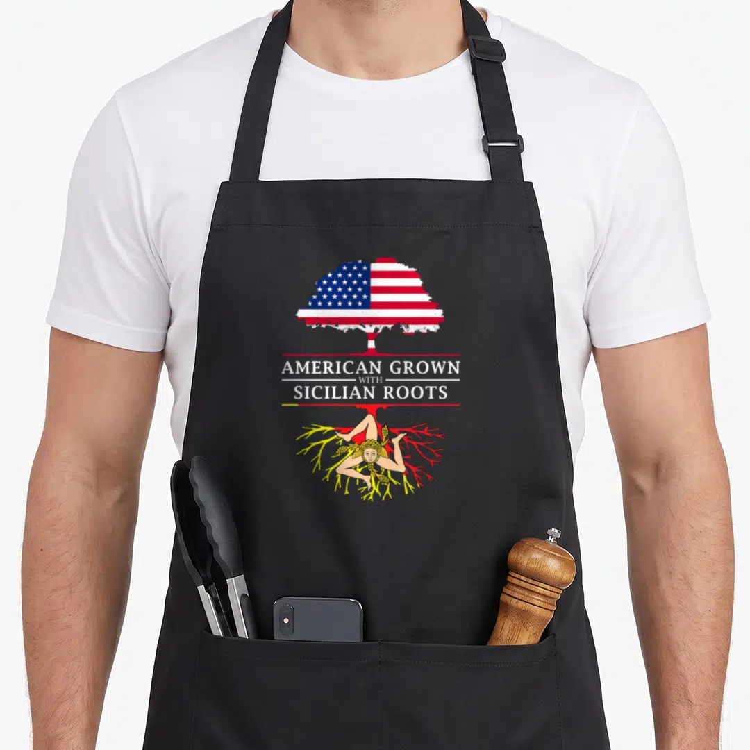 Grown sicily apron - Tree with US flag canopy, white text, yellow roots, and Sicilian figure — shown on a black cotton canvas apron against a white background