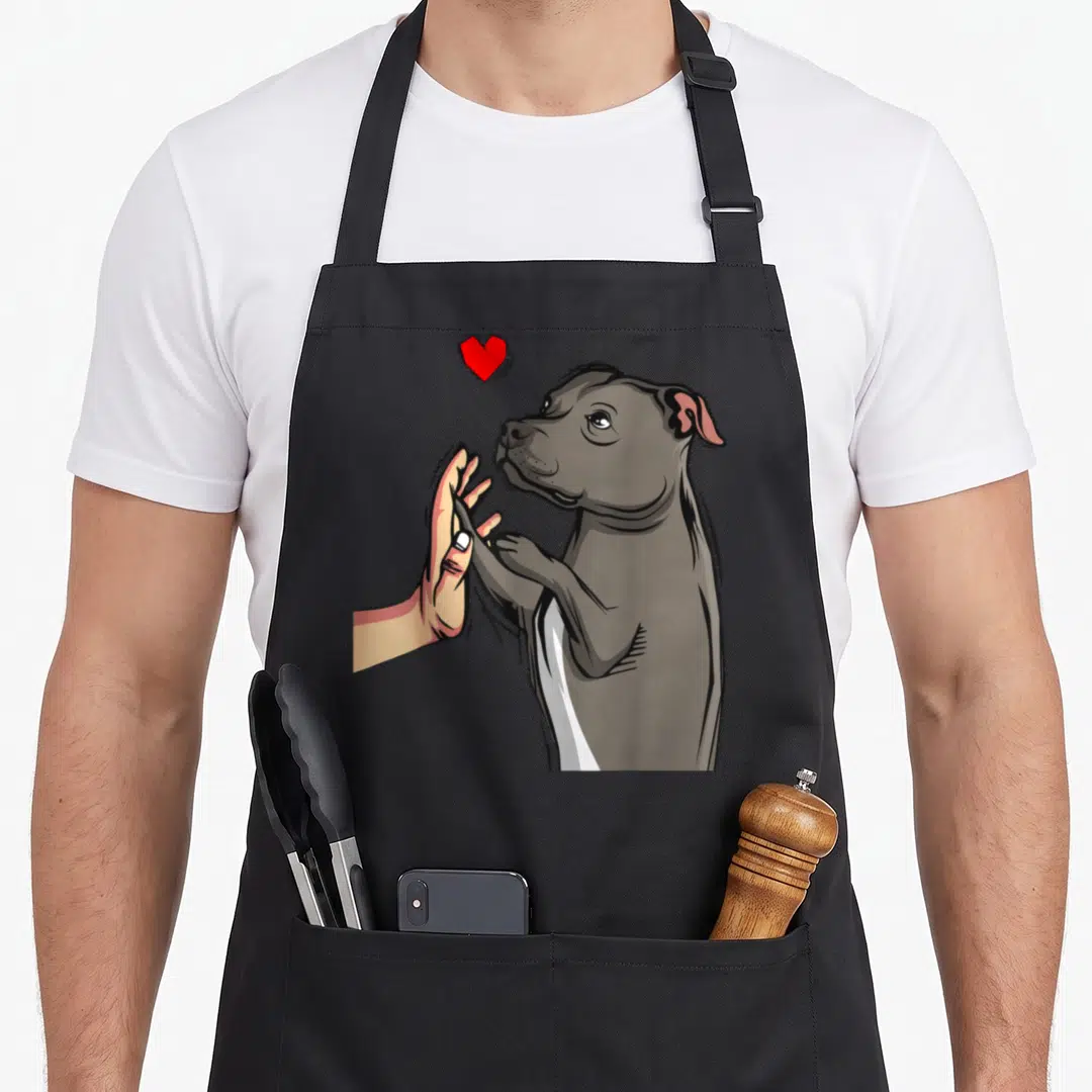 Staffordshire bull dog dad apron - Grey cartoon dog high-fiving a human hand with a red heart floating above its head — shown on a black cotton canvas apron against a white background