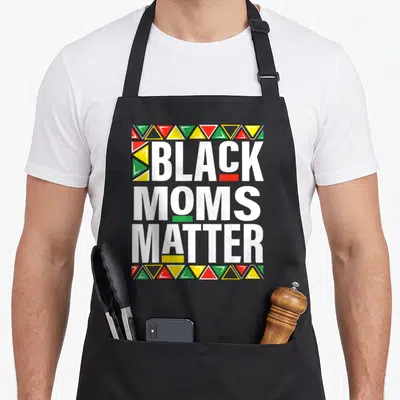 Matter mother's apron - Stacked white text BLACK MOMS MATTER with red yellow green triangles and colored blocks under C — shown on a black cotton canvas apron against a white background