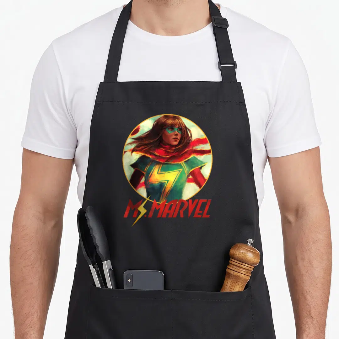 Pose super hero aprons - Realistic Ms. Marvel portrait in yellow circle with red text and lightning bolt on black fabric — shown on a black cotton canvas apron against a white background