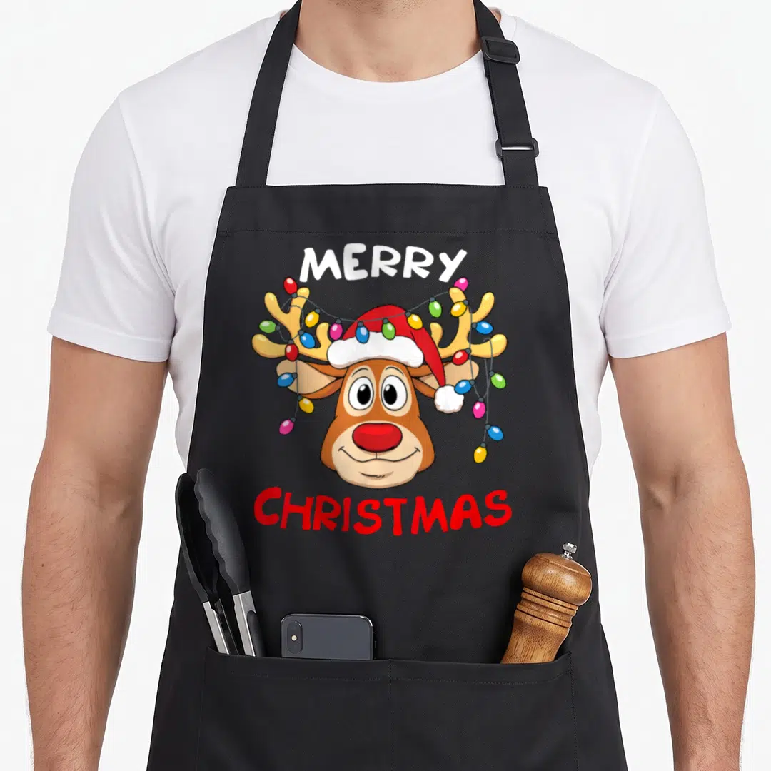Reindeer merry christmas apron - Cartoon reindeer head with Santa hat and colorful lights, Merry Christmas text — shown on a black cotton canvas apron against a white background