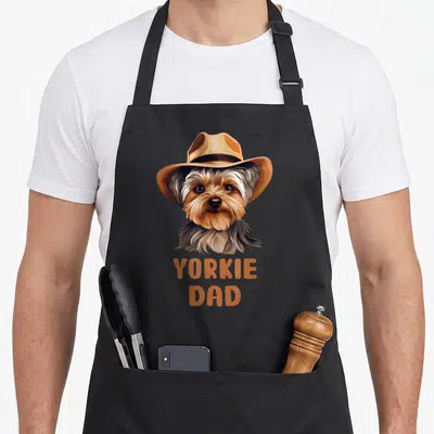 Yorkie puppy dog apron - Realistic Yorkie in tan cowboy hat with orange YORKIE DAD text — shown on a black cotton canvas apron against a white background