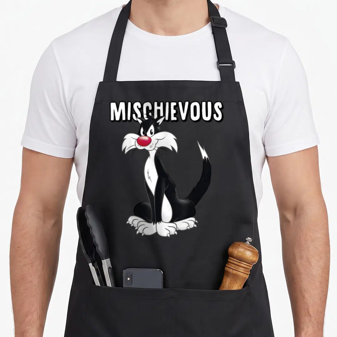 Sylvester cat apron - MISCHIEVOUS text above a seated black and white cartoon cat with a red nose — shown on a black cotton canvas apron against a white background