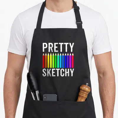 Sketchy pretty apron - Row of 11 colored pencils between pretty and sketchy text — shown on a black cotton canvas apron against a white background