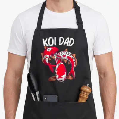 Koi fish japan apron - KOI DAD text above three red white grey koi fish swimming in a circle — shown on a black cotton canvas apron against a white background