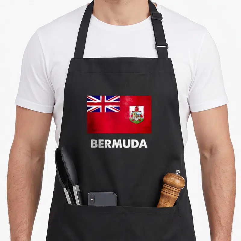 Flag bermuda apron - Distressed red flag with coat of arms above white BERMUDA text on black fabric — shown on a black cotton canvas apron against a white background