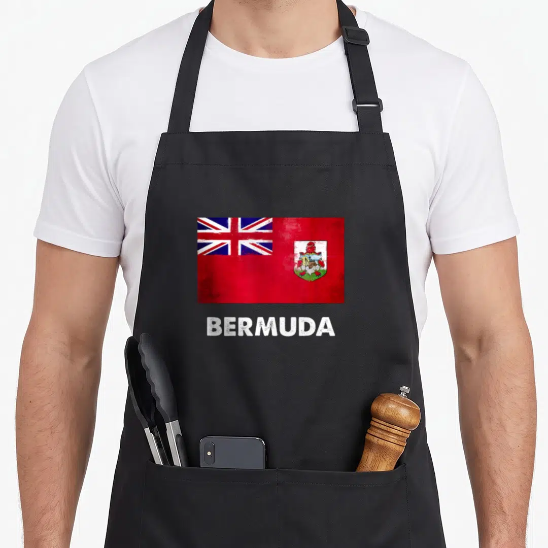 Flag bermuda apron - Distressed red flag with coat of arms above white BERMUDA text on black fabric — shown on a black cotton canvas apron against a white background