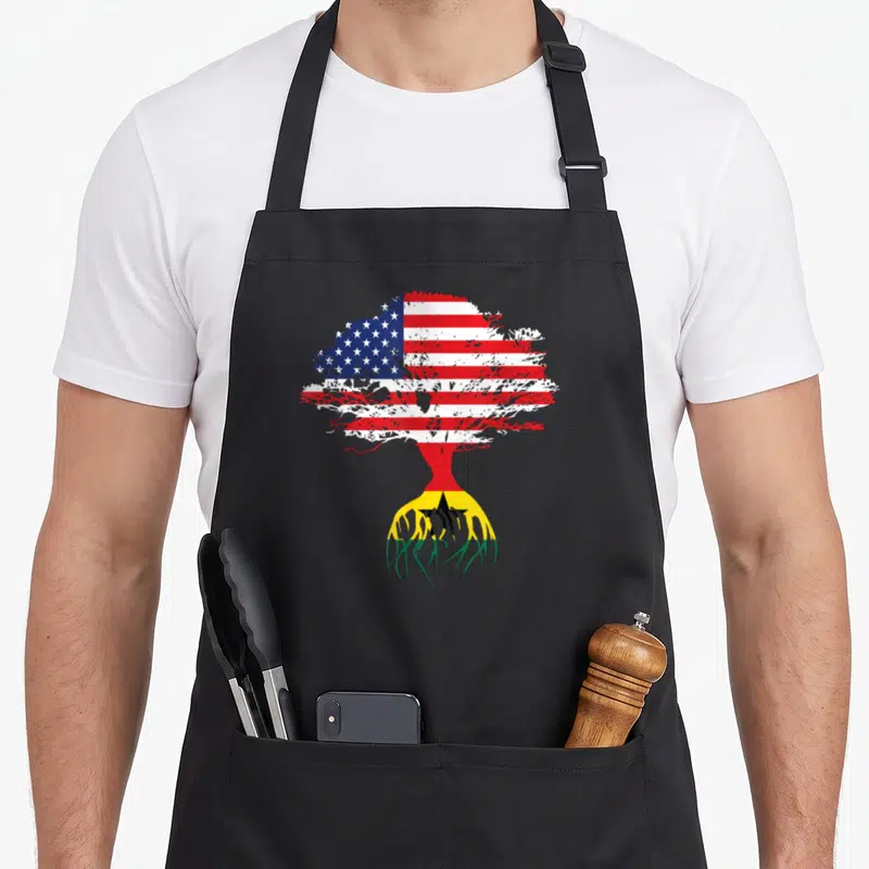 Ghanaian american flag apron - Tree with US flag canopy and Ghana flag roots in red white blue yellow green — shown on a black cotton canvas apron against a white background