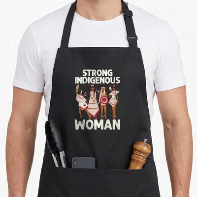 Indigenous aboriginal native american apron - Four indigenous women in traditional dress holding a bird, shield — shown on a black cotton canvas apron against a white background
