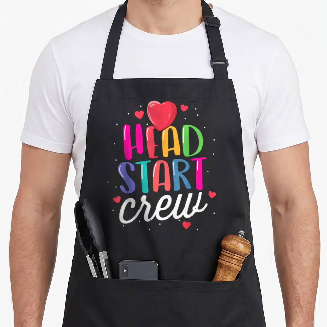 Start preschool teacher apron - stacked HEAD START crew text in pink yellow green blue red and white with hearts — shown on a black cotton canvas apron against a white background