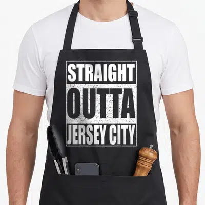 Straight patriotic apron - Stacked white and grey text reading STRAIGHT OUTTA JERSEY CITY inside a rectangular border — shown on a black cotton canvas apron against a white background