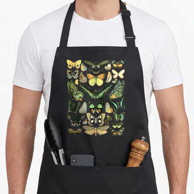 Inspired butterfly apron - Realistic chart of yellow, green, orange, and black butterflies and moths in a dense — shown on a black cotton canvas apron against a white background
