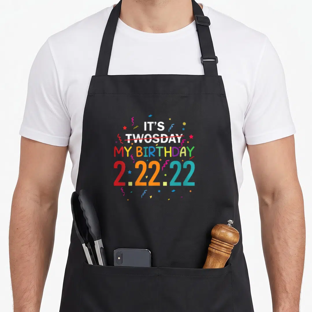 Twosday 2nd apron - Stacked text reading It's My Birthday 2.22.22 with confetti and strike-through — shown on a black cotton canvas apron against a white background