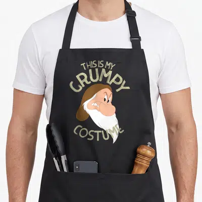 Costume snow white apron - Cartoon grumpy dwarf head with THIS IS MY GRUMPY COSTUME text in beige arching above — shown on a black cotton canvas apron against a white background