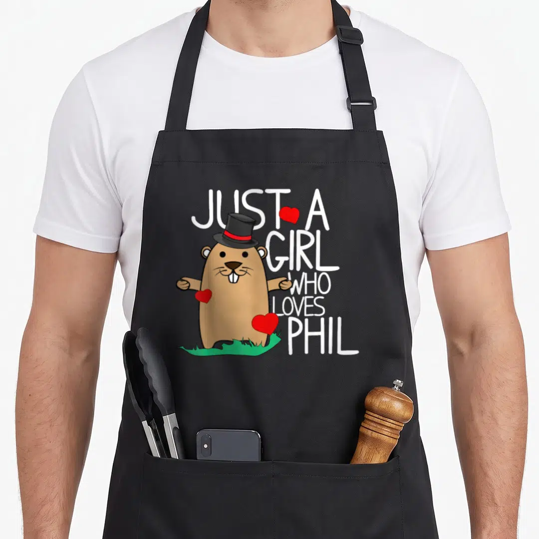 Punxsy holiday apron - Cartoon brown beaver in top hat with white text and red hearts on green grass — shown on a black cotton canvas apron against a white background