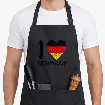 Germany pride german apron - I GERMANY text below black red and yellow striped heart in sketch style — shown on a black cotton canvas apron against a white background