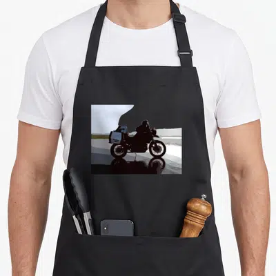 Vintage motorcycle bike apron - Minimalist silhouette of a motorcycle rider reflecting in wet sand using black grey — shown on a black cotton canvas apron against a white background