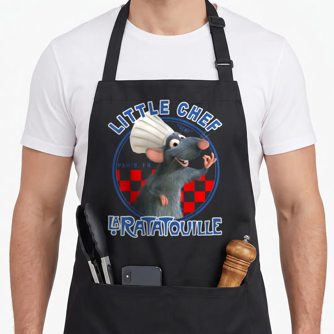 Badge remy ratatouille apron - Remy rat wearing chef hat inside blue circle with red checkered background and LITTLE — shown on a black cotton canvas apron against a white background
