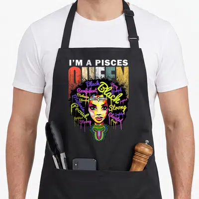 Pisce february birthday apron - Cartoon woman with afro surrounded by colorful text reading Pisces Queen Strong Proud — shown on a black cotton canvas apron against a white background