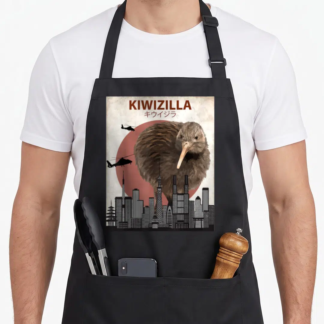 Kiwizilla new zealand apron - Giant brown kiwi bird over city skyline with helicopters and KIWIZILLA text — shown on a black cotton canvas apron against a white background