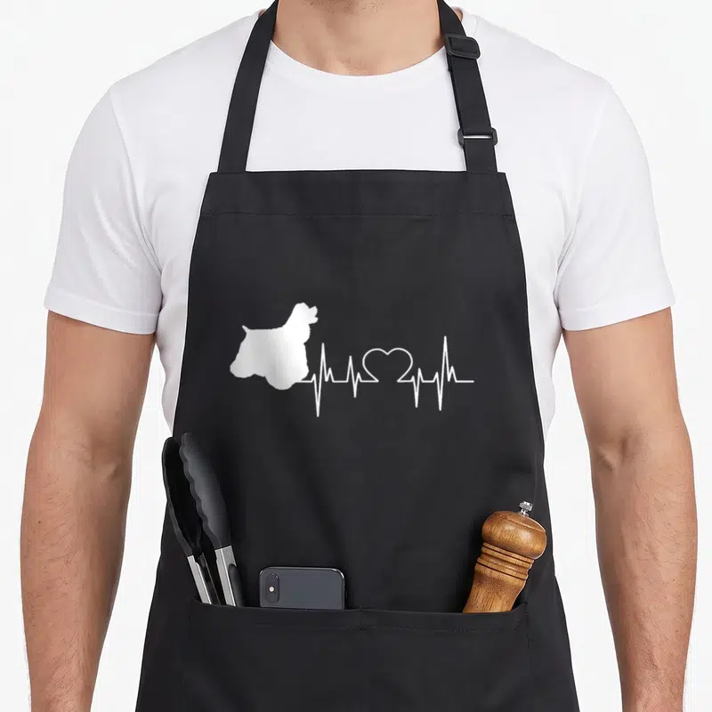 Heartbeat cocker spaniel apron - White dog silhouette connected to heartbeat line with heart shape in center — shown on a black cotton canvas apron against a white background