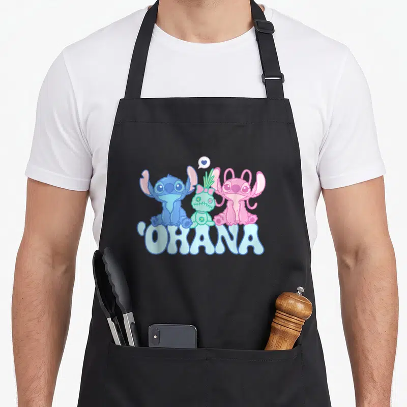 Scrump angels in aprons - Three cartoon aliens in blue pink green sit above OHANA text with heart bubble — shown on a black cotton canvas apron against a white background