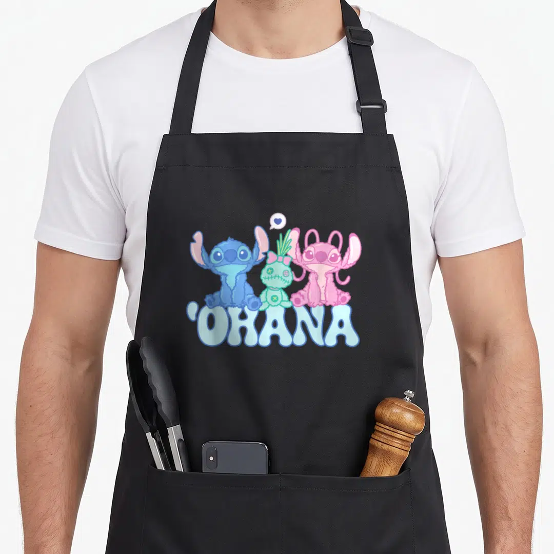 Scrump angels in aprons - Three cartoon aliens in blue pink green sit above OHANA text with heart bubble — shown on a black cotton canvas apron against a white background
