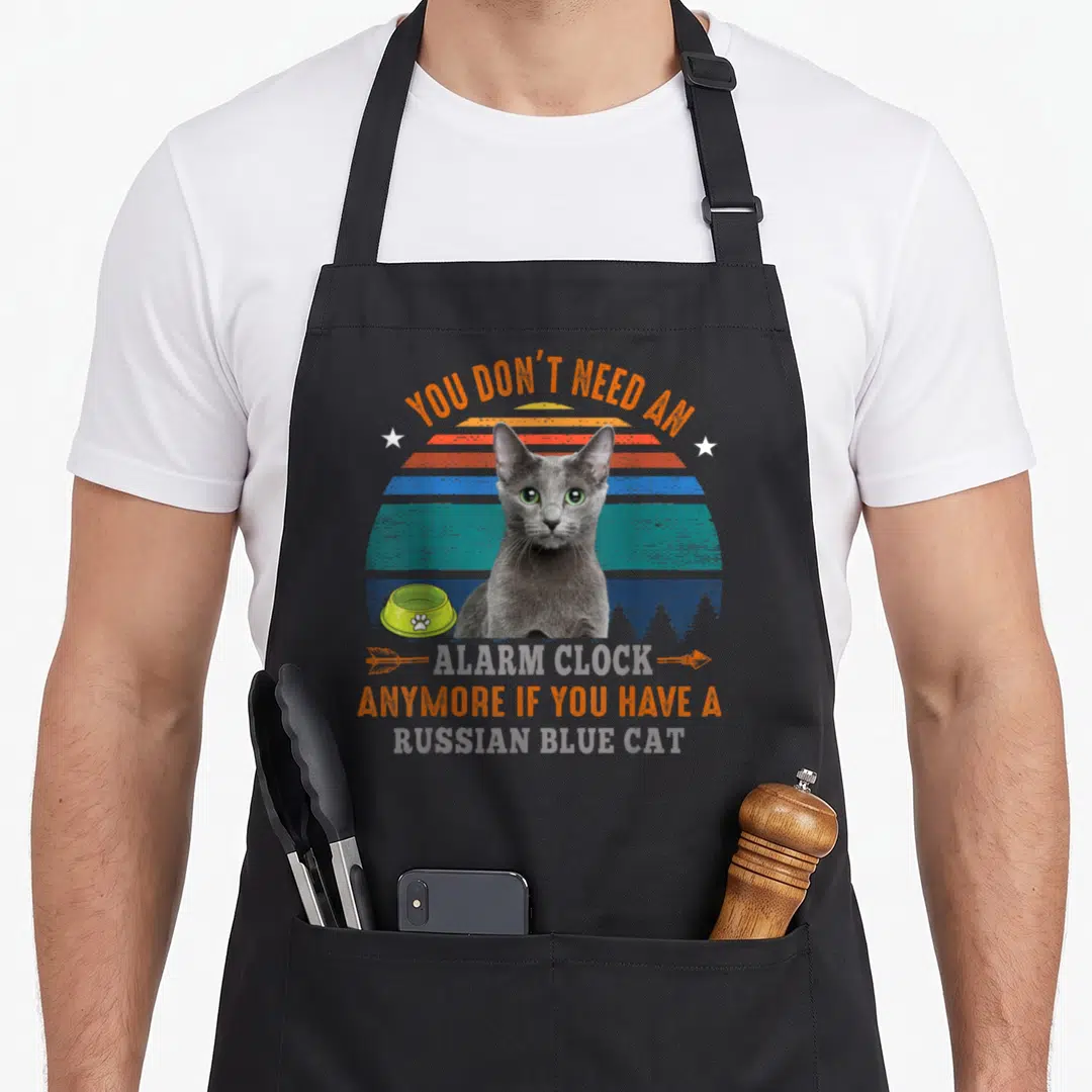 Alarm russian aprons - Grey Russian Blue cat in front of orange blue and teal striped sunset with food bowl and printed — shown on a black cotton canvas apron against a white background