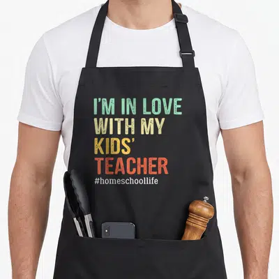 Mama cute teacher apron - Stacked I'M IN LOVE WITH MY KIDS' TEACHER text in mint beige yellow orange white — shown on a black cotton canvas apron against a white background