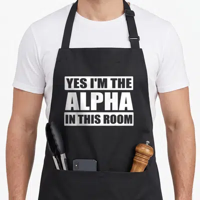 Confident alpha apron - Stacked white text YES I'M THE ALPHA IN THIS ROOM on grey blocks — shown on a black cotton canvas apron against a white background