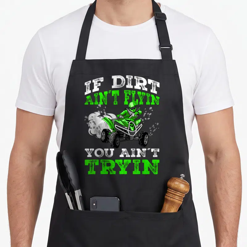 Dirt wheeler apron - ATV rider with IF DIRT AIN'T FLYIN YOU AIN'T TRYIN text in green and white distressed font — shown on a black cotton canvas apron against a white background