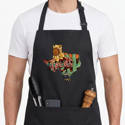 Sunflower cactus apron - Texas map filled with sunflower, cacti, and patterns in cartoon style — shown on a black cotton canvas apron against a white background