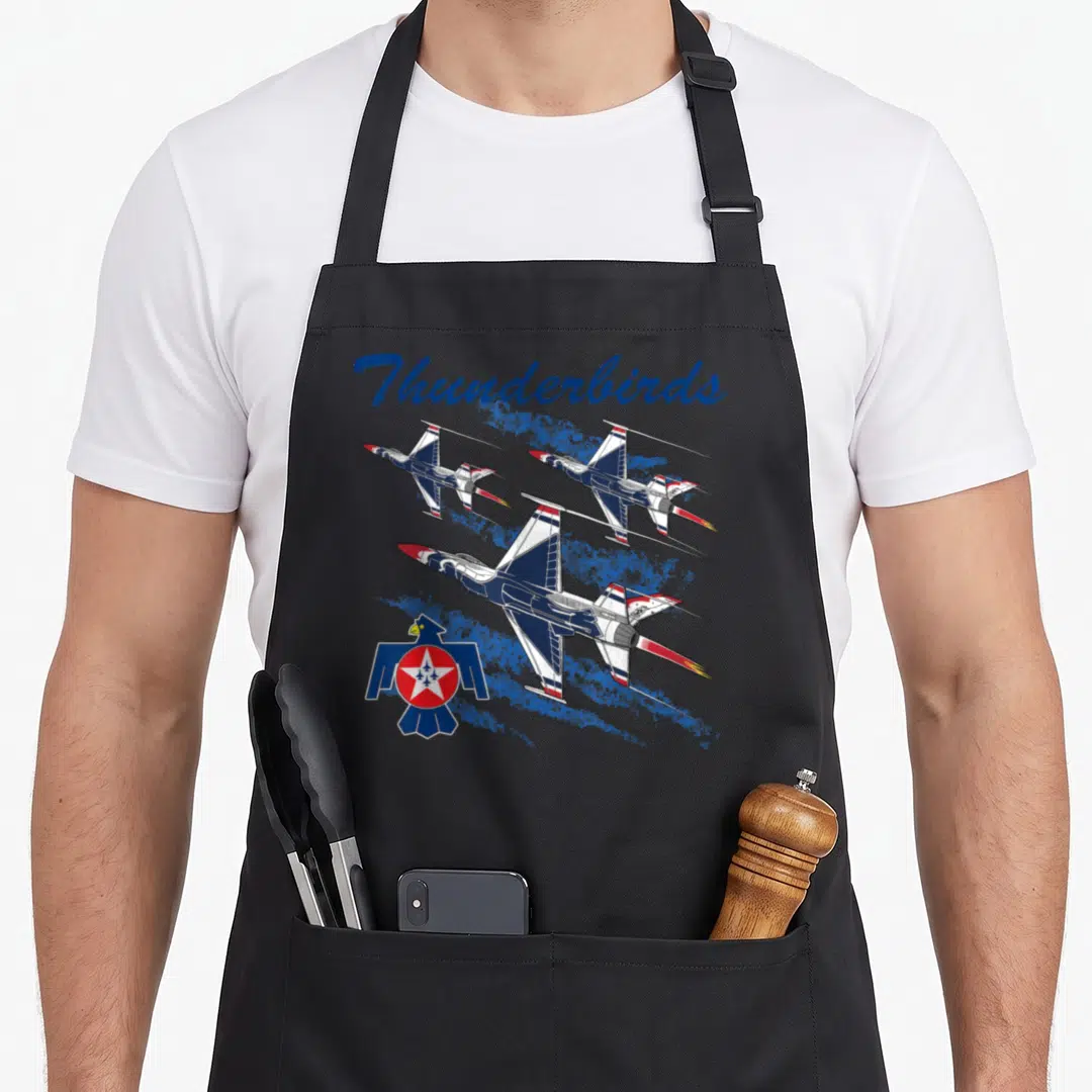 Thunderbird aviation apron - Three jets in formation with Thunderbirds text and bird logo over blue splatters — shown on a black cotton canvas apron against a white background