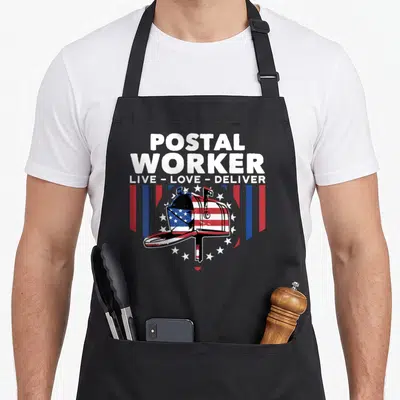 Deliver postal aprons - Stacked postal worker text above a flag-patterned mailbox flanked by red white blue stripes — shown on a black cotton canvas apron against a white background