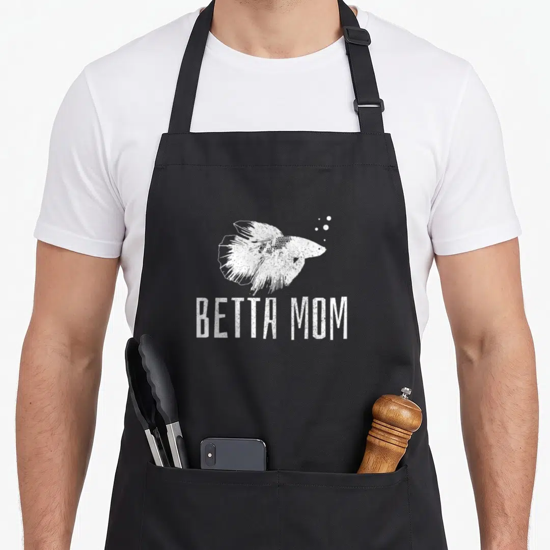Splenden fish apron - White distressed betta fish illustration above Betta Mom text with small bubbles — shown on a black cotton canvas apron against a white background