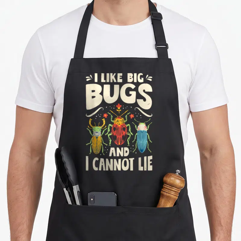 Cannot entomologist apron - Three cartoon beetles in red blue and yellow under text I Like Big Bugs And I Cannot Lie — shown on a black cotton canvas apron against a white background