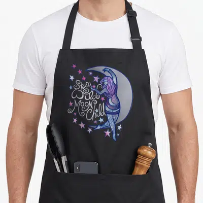 Goddess moon child apron - Stay Wild Moon Child text over woman leaning on crescent moon with pink and blue stars — shown on a black cotton canvas apron against a white background