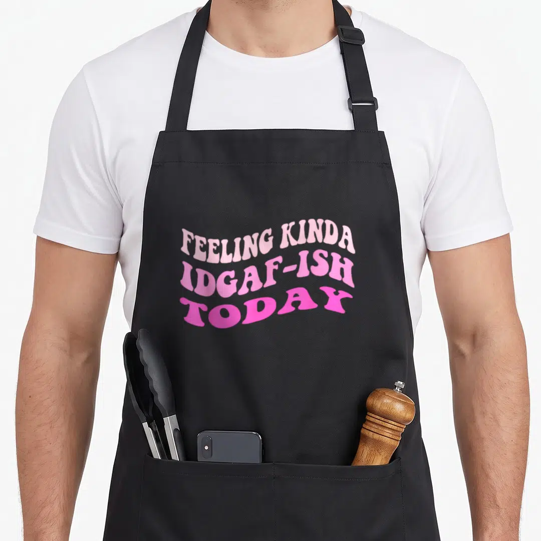 Groovy snarky aprons - Wavy pink typography reading Feeling Kinda Idgaf-ish Today stacked in three lines — shown on a black cotton canvas apron against a white background