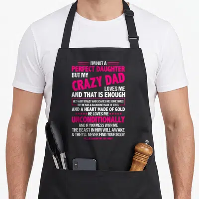 But dad and daughter aprons - Pink and white typography reading I'm not a perfect daughter but my crazy dad loves me — shown on a black cotton canvas apron against a white background