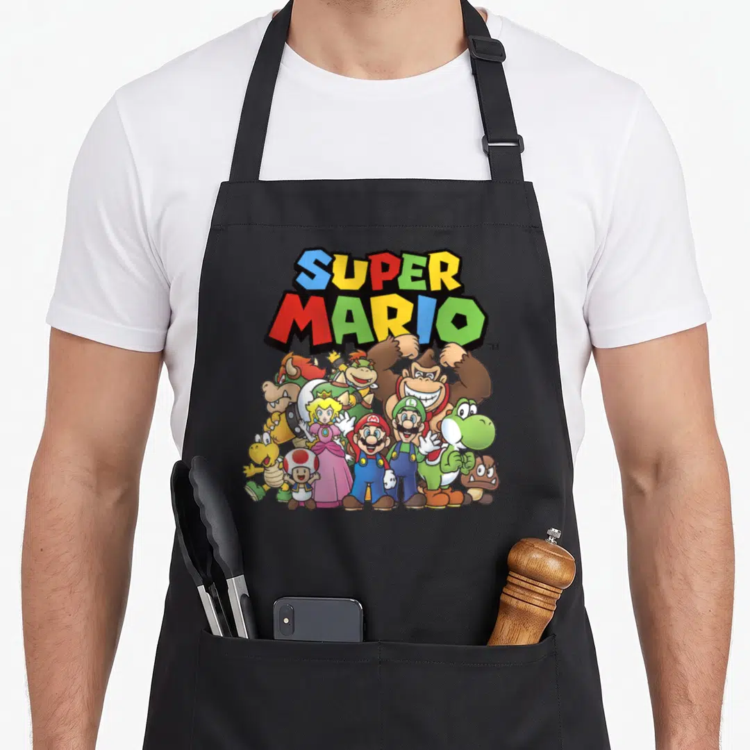 Cast shot apron - SUPER MARIO text above Mario Luigi Peach Yoshi Donkey Kong Bowser Toad Goomba yellow creature — shown on a black cotton canvas apron against a white background