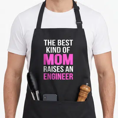 Kind mother's apron - Stacked text reading THE BEST KIND OF MOM RAISES AN ENGINEER in white and pink block letters — shown on a black cotton canvas apron against a white background