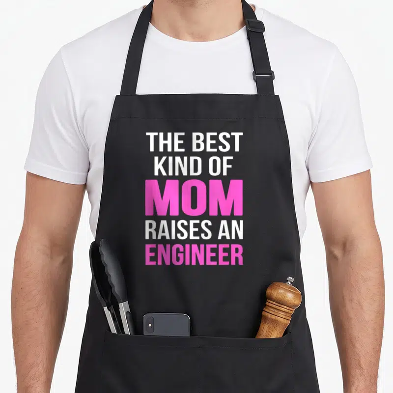 Kind mother's apron - Stacked text reading THE BEST KIND OF MOM RAISES AN ENGINEER in white and pink block letters — shown on a black cotton canvas apron against a white background