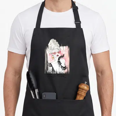 Queen french style apron - Cartoon woman in pink sunglasses and black gloves with Marie Antoinette script text on pink — shown on a black cotton canvas apron against a white background