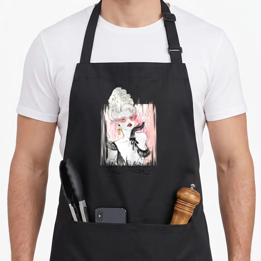 Queen french style apron - Cartoon woman in pink sunglasses and black gloves with Marie Antoinette script text on pink — shown on a black cotton canvas apron against a white background