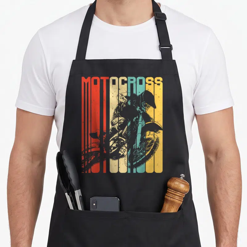 Motocross dirt rider bike apron - MOTOCROSS text over grey rider silhouette on vertical red orange yellow green blue — shown on a black cotton canvas apron against a white background