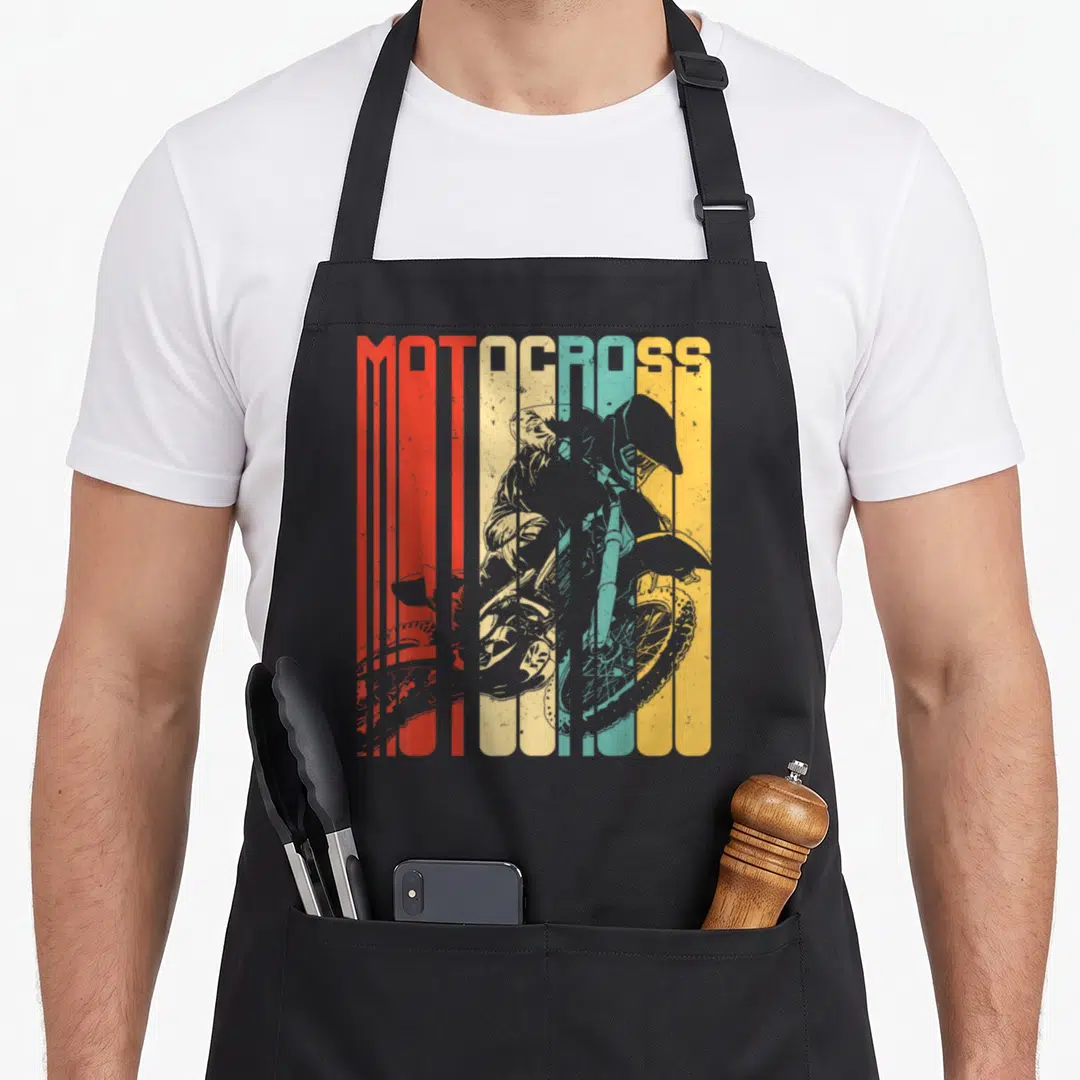 Motocross dirt rider bike apron - MOTOCROSS text over grey rider silhouette on vertical red orange yellow green blue — shown on a black cotton canvas apron against a white background
